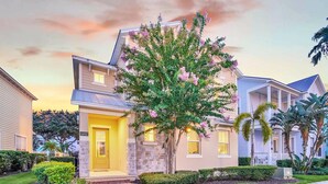 A two-story house with a stone facade, a front porch, and a well-maintained lawn. - Charming Retreat at Reunion | 5BR/5BA Villa, Private Pool, Arcade, Themed Kids Rooms & Golf Access (Kissimmee)