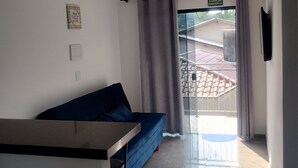 A modern living room with a blue sofa, a small table, and a sliding glass door leading to a balcony. - Pousada da Família com Apartamentos Mobiliados e Completos! (Santa Lidia Penha)