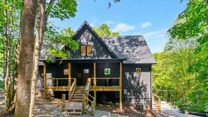 A cabin with a dark exterior, wooden deck, and a staircase leading to the entrance.