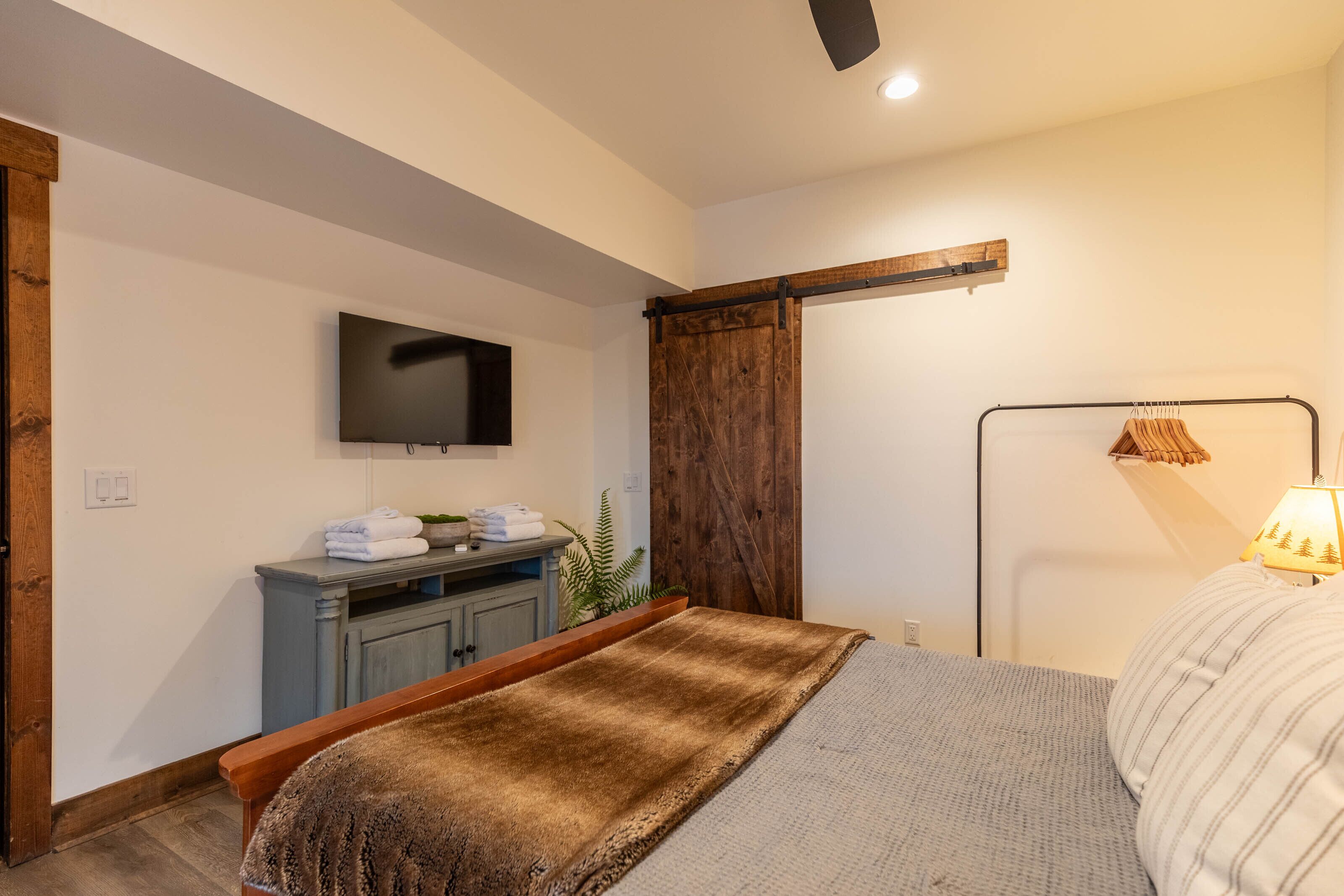 A bedroom with a bed, a TV mounted on the wall, a wooden wardrobe, and a sliding door.