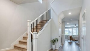 Eine Treppe mit beigefarbenen Teppichstufen und weißen Geländern, die zu einem Flur mit Holzboden und einem Blumentopf führt.