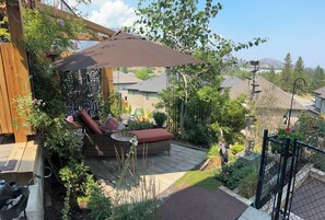 A patio with a wicker lounge chair, a table, and a pergola with a brown umbrella. - Shannon Ridge Mountain View Home (West Kelowna)