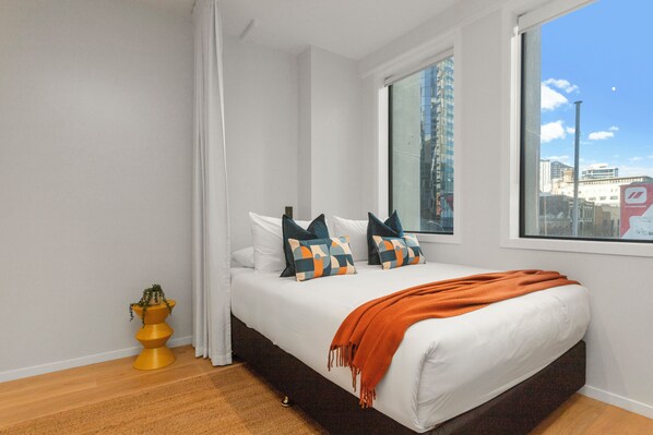Un dormitorio moderno con una cama, un ventanal con vista a la ciudad y una mesita de noche amarilla.