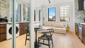 A modern kitchen with a dining area, a washing machine, and a sofa. - Victoria Street Apartments (Auckland)