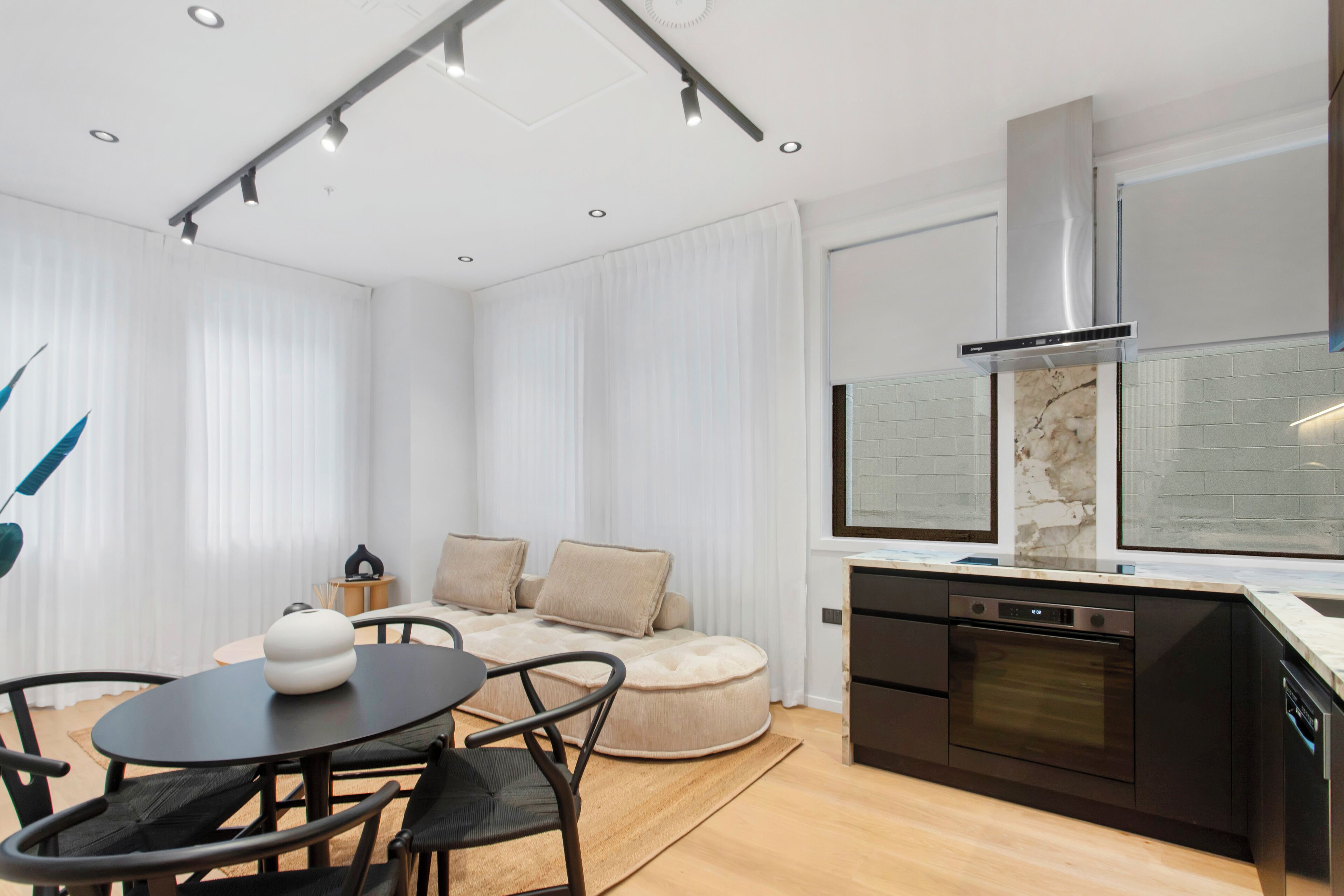 A modern kitchen with a built-in oven and dishwasher, a dining area with a round table and chairs, and a cozy seating area with a sofa and cushions.