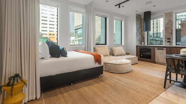 A modern hotel room with a large bed, a sofa, a dining table, and a kitchen area. - Victoria Street Apartments (Auckland)