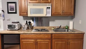 A compact kitchen with wooden cabinets, a microwave, a toaster, and a sink.