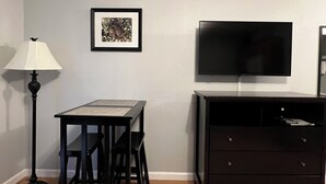 A small room with a desk, chairs, a lamp, a television, and a dresser.