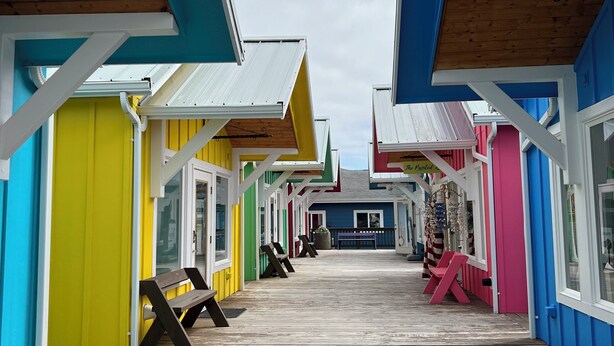 A wooden boardwalk leading to colorful buildings with large windows and a clear sky above.