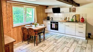 Una cocina con armarios de madera, una mesa de comedor con sillas, un ventanal con vistas a la vegetación y un horno empotrado.