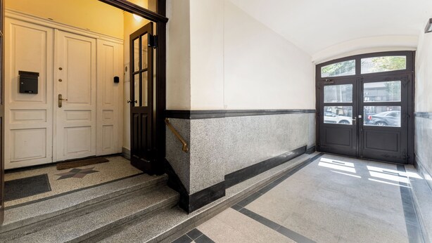 Una entrada limpia y moderna con piso de mármol, puerta con marco negro y pared blanca con un ventanal pequeño.