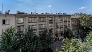 Un edificio de varios pisos con balcones y ventanas, rodeado de árboles y coches estacionados.