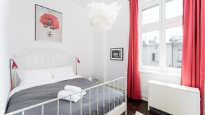 Un dormitorio ordenado con cama, radiador, ventana con cortinas y una obra de arte colgada en la pared.
