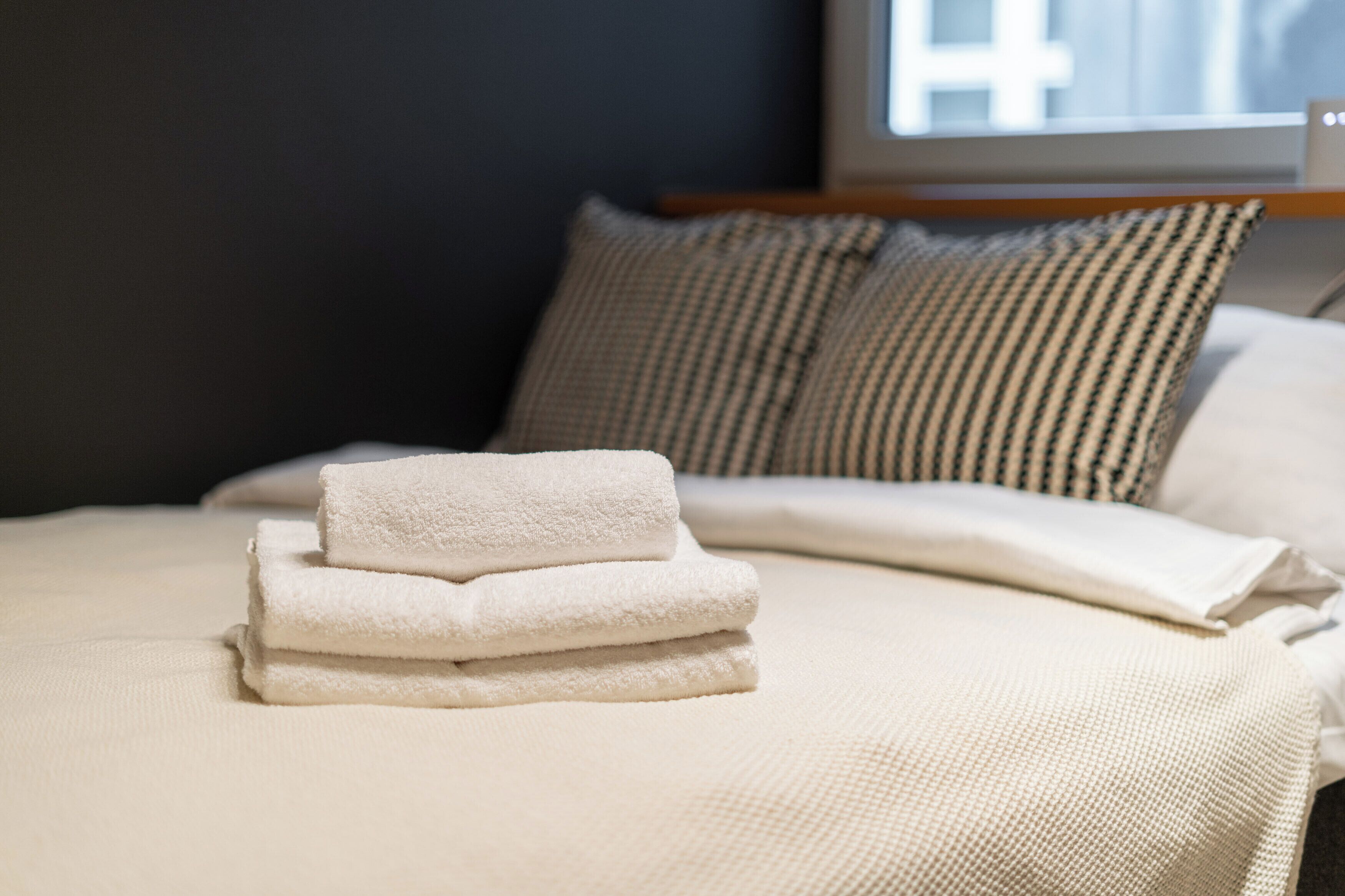 A neatly made bed with a white comforter and two folded white towels.