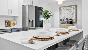 A modern kitchen with white cabinetry, a stainless steel refrigerator, and a central island with white plates and woven placemats.