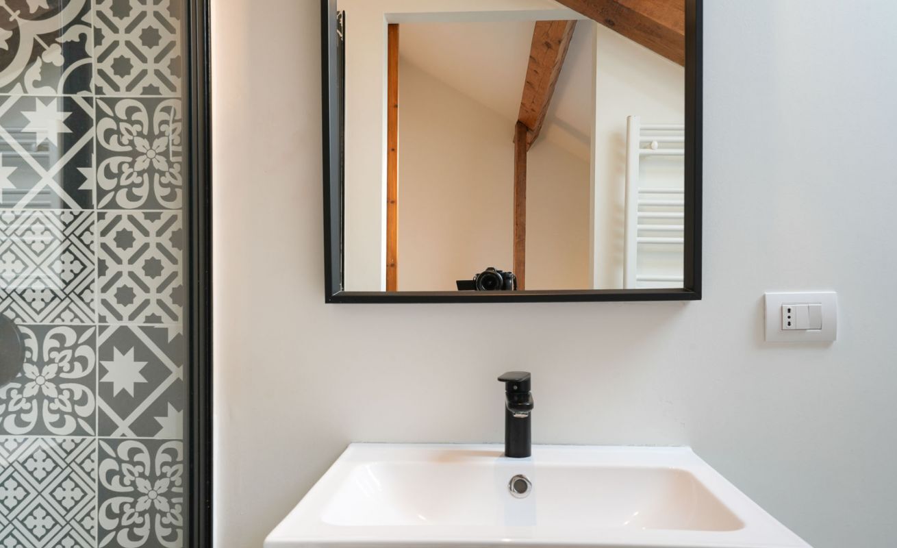 A bathroom with a white sink, a black faucet, and a mirror reflecting a wooden ceiling and a white towel rack.