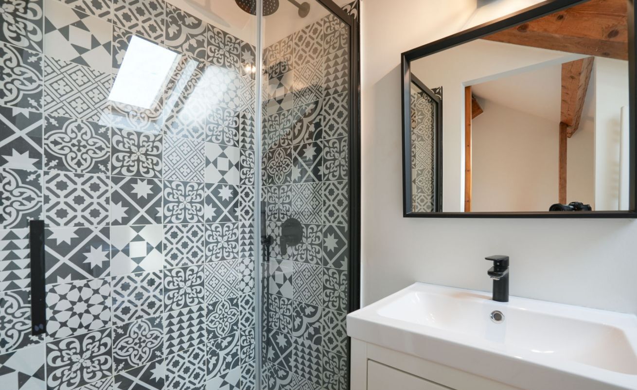 A bathroom with patterned tiles, a white sink, and a mirror with a wooden beam above.