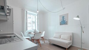 A modern kitchen with a built-in stove, a dining area with white chairs, a white sofa, and a floor lamp. - [Torino Centro] Odissea House (Torino)
