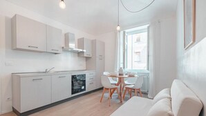 A modern kitchen with white cabinets, a dining table with chairs, and a sofa in a bright room with a window. - [Torino Centro] Odissea House (Torino)