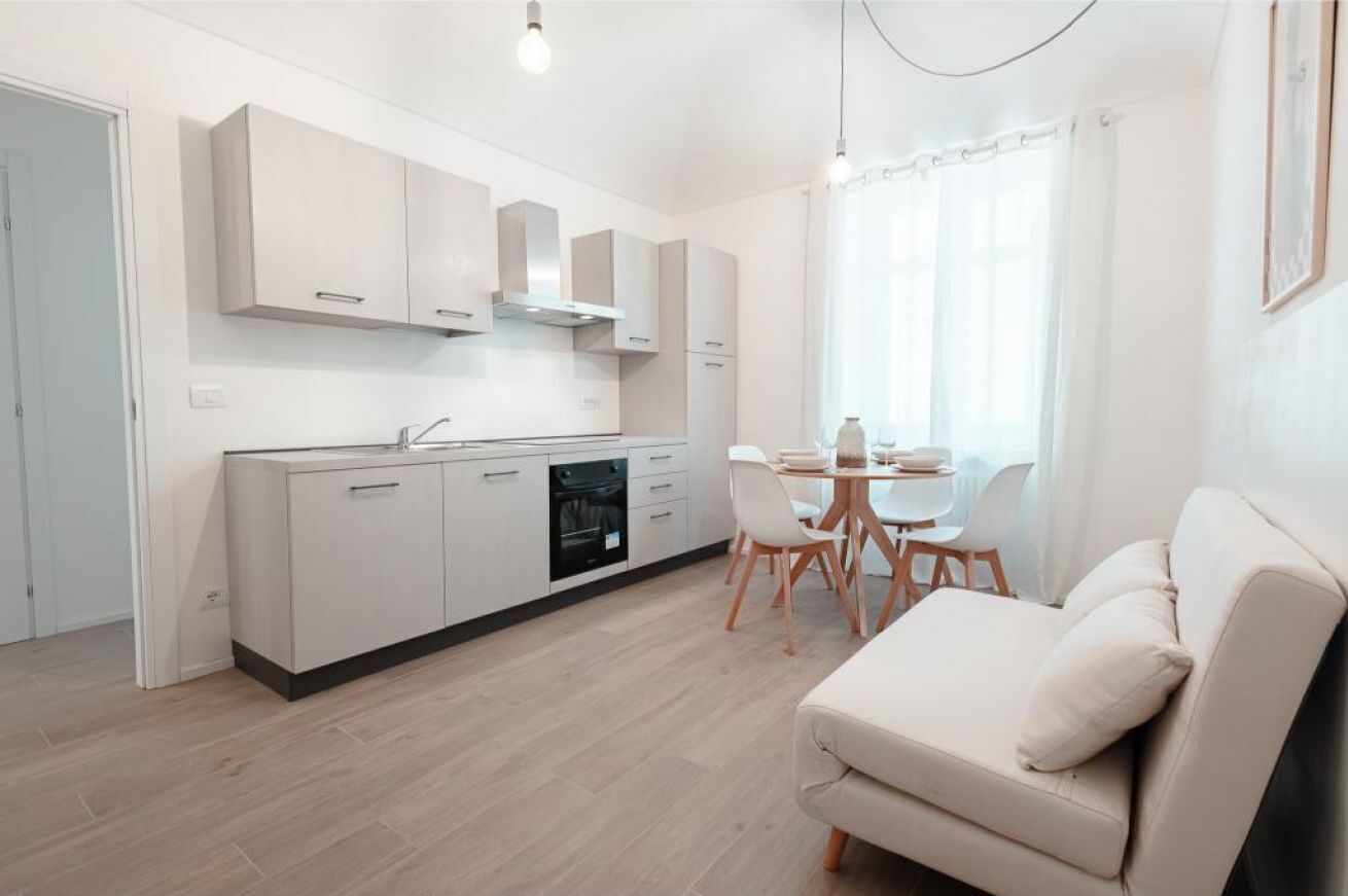A modern kitchen with white cabinets, a dining area with a table and chairs, and a sofa.