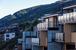 Ein modernes Mehrfamilienhaus mit großen Balkonen, Holzverkleidung und Blick auf eine bewaldete Hügelslandschaft.