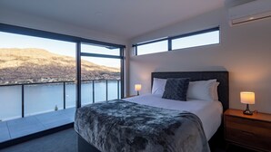 Ein modernes Schlafzimmer mit einem großen Bett, zwei Nachttischen und Blick auf einen See und Berge.