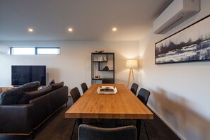 Ein modernes Wohnzimmer mit einem Holzesstisch, einem schwarzen Ledersofa und einem Flachbildfernseher.