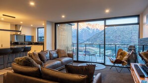 Ein modernes Wohnzimmer mit Ledersofa, Essbereich und Bergblick durch große Fenster.