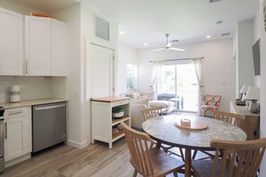 A modern kitchen with white cabinets, a dishwasher, and a dining area with a round table and chairs. - Modern 2 bed with pool and gym (West Bay)