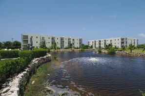 A modern hotel with a pool, surrounded by greenery and a clear sky. - Modern 2 bed with pool and gym (West Bay)