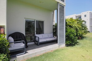 Un espacio al aire libre con techo, con puerta corredera de vidrio, un sofá blanco y una parrilla.