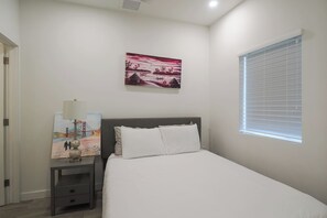 Un dormitorio con cama, mesita de noche, lámpara y ventana con persianas.