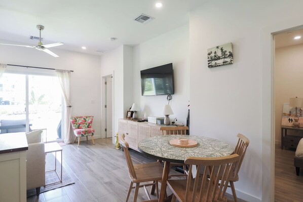 Comedor con una mesa redonda, sillas, televisor montado en la pared y vista al exterior a través de una ventana.