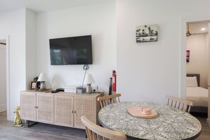 A dining area with a round table, chairs, a television mounted on the wall, and a small cabinet with decorative items. - Modern 2 bed with pool and gym (West Bay)