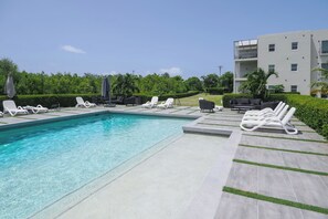 Una piscina con sillones reclinables y un edificio moderno al fondo.
