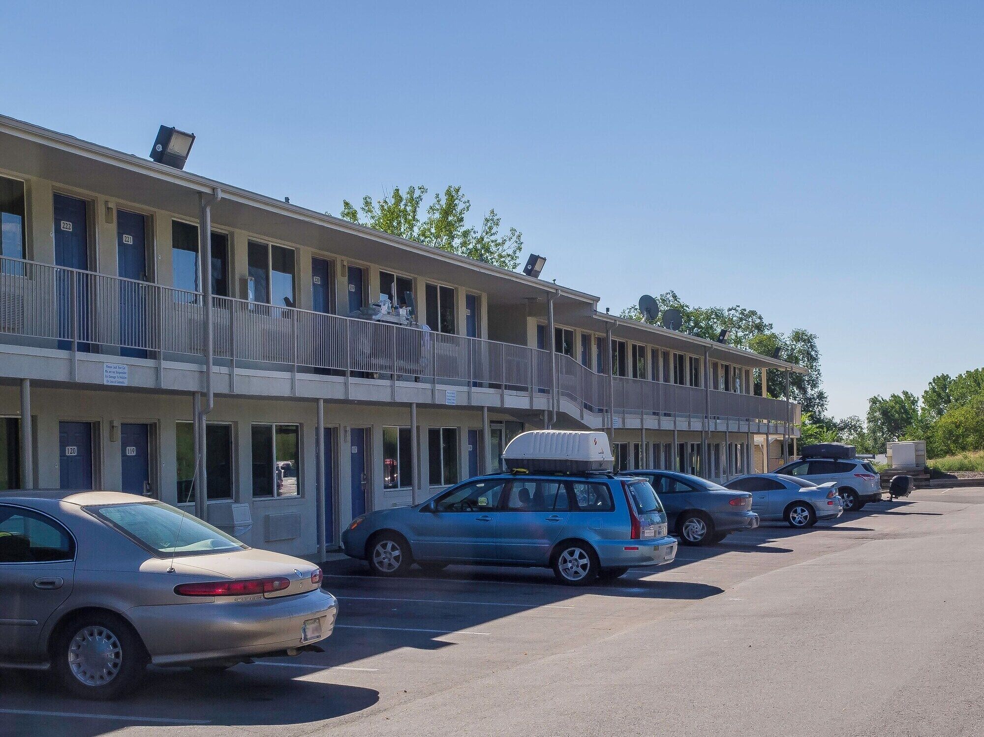A multi-story motel with numbered rooms, a parking lot, and a clear sky.