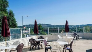 An outdoor patio with tables and chairs, umbrellas, and a view of the cityscape. - Motel 6 – Colorado Springs, CO – South/Metro Area (Colorado Springs)