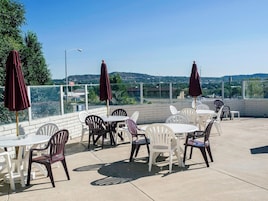 Un patio al aire libre con mesas, sillas y sombrillas, y vista del paisaje urbano.