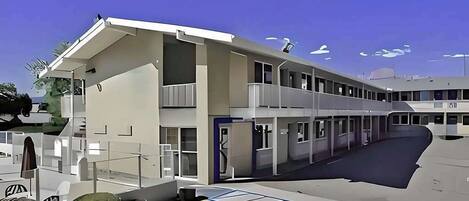 Un edificio moderno con techo plano, varios balcones y un estacionamiento con espacios delimitados.