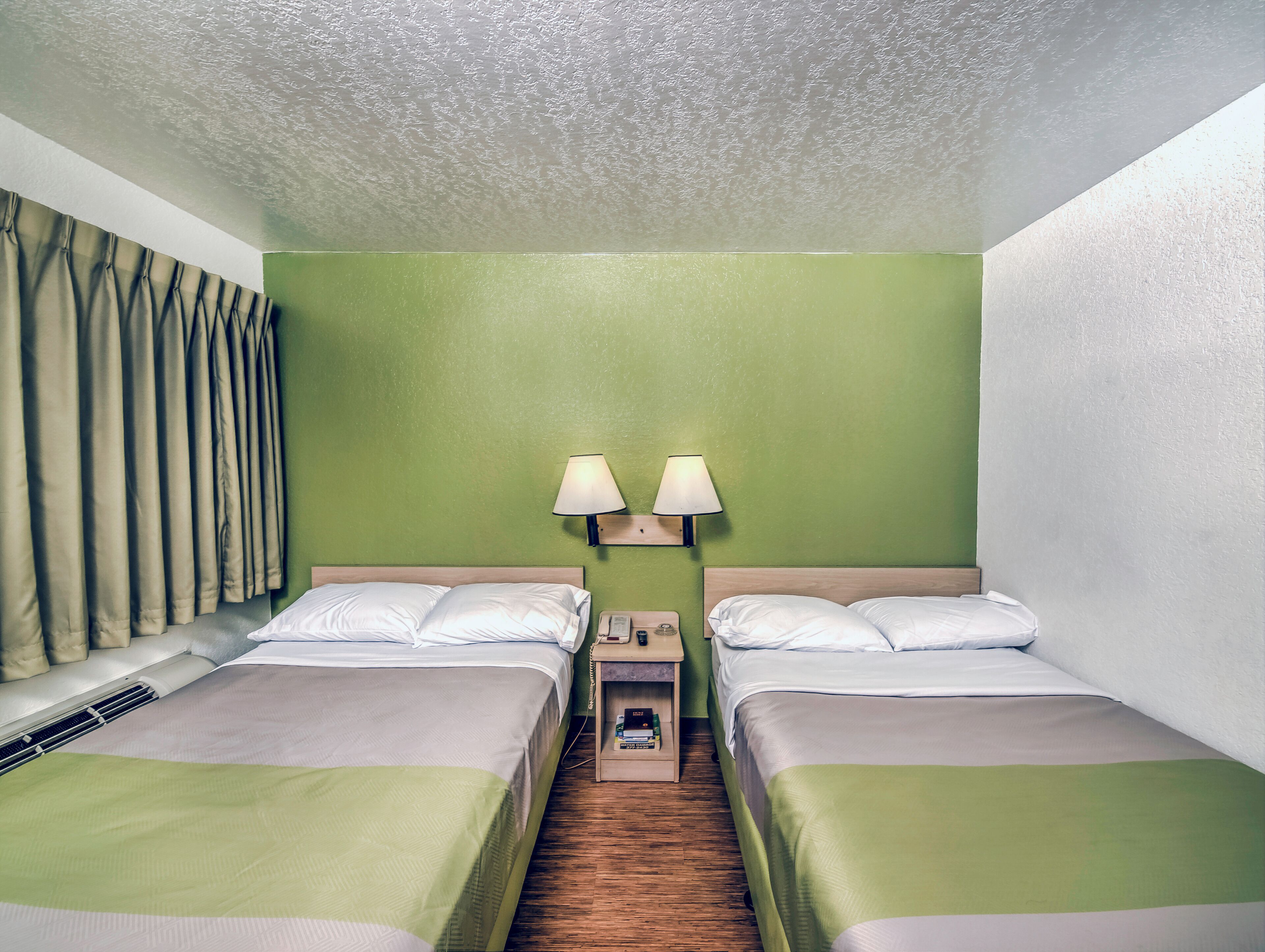 A hotel room with two beds, a nightstand with a lamp, and a telephone.