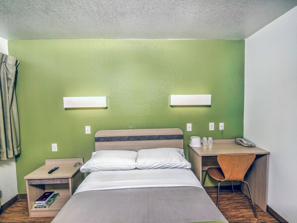 Habitación de hotel con cama, mesita de noche, escritorio con silla y dos lámparas de pared.