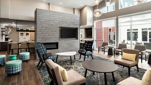 A modern lounge area with a fireplace, comfortable seating, and a large window offering a view of the city. - Residence Inn by Marriott Mechanicsburg (Enola)