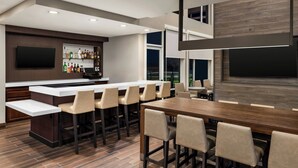 A modern kitchen with a bar area, a dining table with chairs, and a large TV mounted on the wall. - Residence Inn by Marriott Mechanicsburg (Enola)
