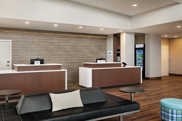 A hotel reception area with two reception desks, a black leather sofa, a small round table, and a vending machine. - Residence Inn by Marriott Mechanicsburg (Enola)