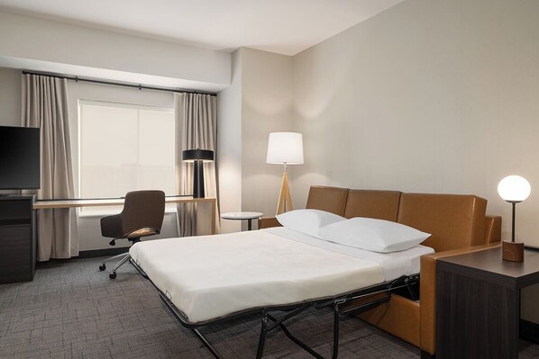 A hotel room with a bed, a desk, a chair, a TV, a lamp, and a window with curtains. - Residence Inn by Marriott Mechanicsburg (Enola)