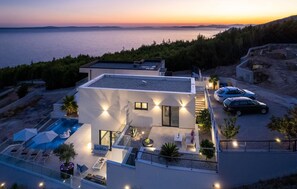 Enjoy the rooftop pool and outdoor seating area with a sofa and chairs, surrounded by a natural landscape and sea views.