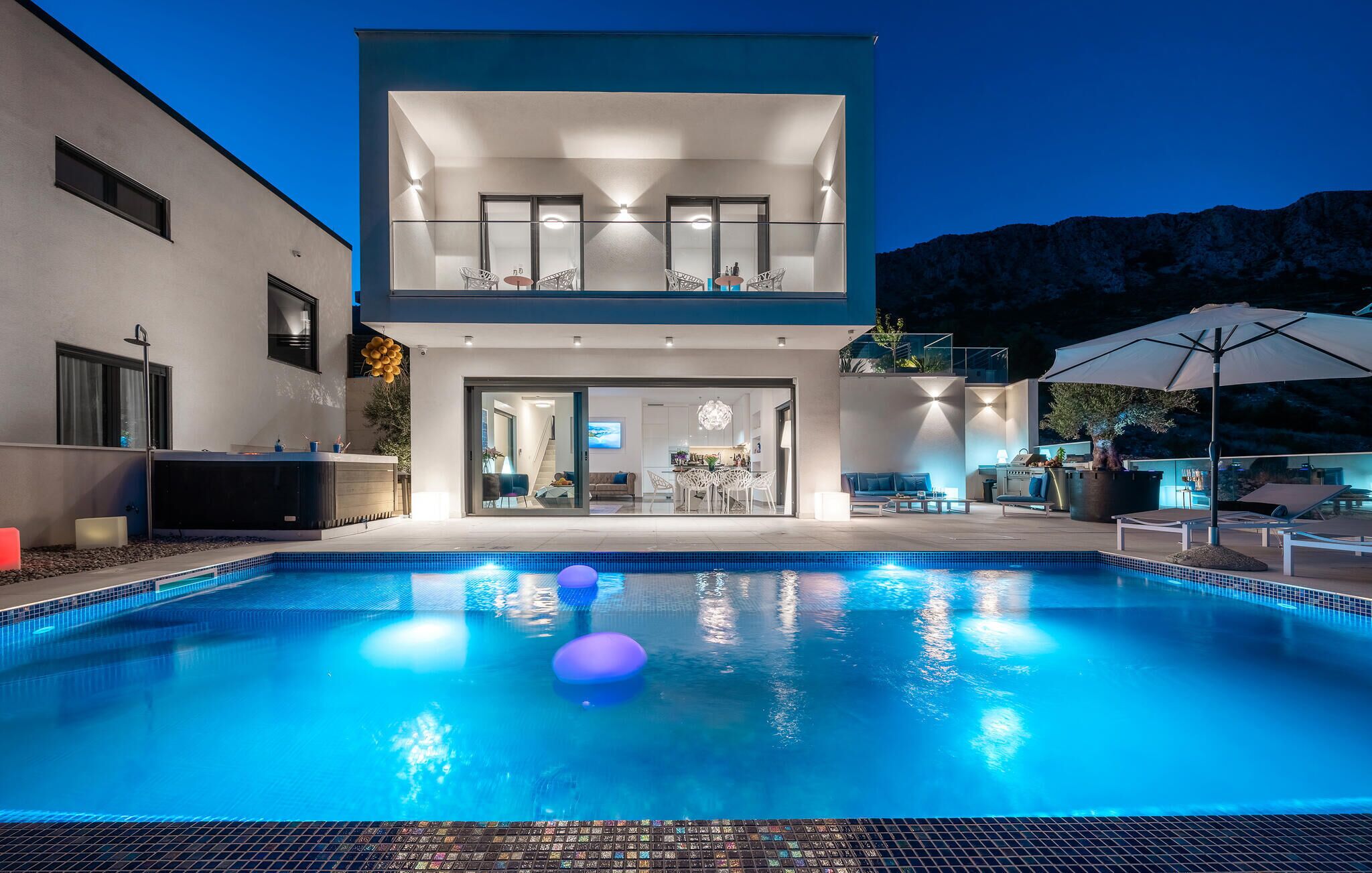 Una casa moderna de dos pisos con piscina, mobiliario exterior y un paisaje de montañas al fondo.