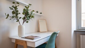 A white desk with a teal chair, a white vase with green leaves, and a framed picture on the wall. - Rooftop View Bilo - Bocconi Area (Milano)