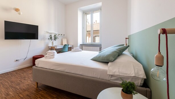A bedroom with a bed, a desk, a chair, a TV mounted on the wall, and a window. - Rooftop View Bilo - Bocconi Area (Milano)