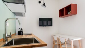 A modern kitchen with a wooden countertop, stainless steel sink, and a kettle. There is a white table with two chairs and a red shelf above it. - Rooftop View Bilo - Bocconi Area (Milano)